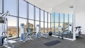 A modern gym with large windows offering city views, various exercise equipment, and a clean, spacious layout. - Cloudview Retreat | Luxe Skyhome Experience (Surfers Paradise)