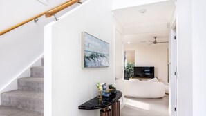 A modern interior with a staircase, a console table, and a living area with a sofa and TV. - 4BR Cozy house 5mins to beach (Surfers Paradise)