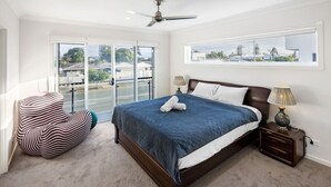 A bedroom with a large bed, a ceiling fan, a window with a view, and a chair by the window. - 4BR Cozy house 5mins to beach (Surfers Paradise)