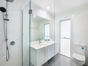 A modern bathroom with a glass shower enclosure, a double sink vanity, and a toilet.