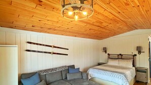 Een gezellige kamer met een houten plafond, een bank, een bed en een klein tafeltje.