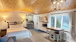 Een gezellig chaletinterieur met een houten plafond, een bed met hoofdeinde, een bank, een eettafel en een keukenhoek.