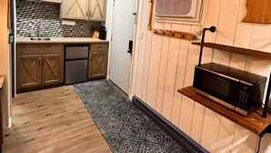 Een keuken met houten kastjes, een decoratieve spatwand, een plank voor een magnetron en een vloerkleed.