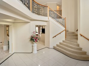 Un interior espacioso con una escalera curva, un pilar blanco adornado con flores y vista a otra habitación.