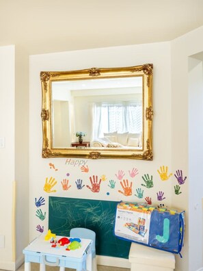 Una habitación infantil con un espejo grande, una mesita con juguetes, una pizarra y huellas de manos de colores en la pared.