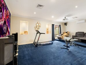 Ein Zimmer mit Laufband, Massagesessel und einem großen Fernseher, der einen Film zeigt.