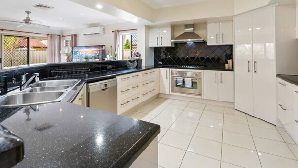 A modern kitchen with a black countertop, white cabinets, and a built-in oven. - Private Cinema! 5Beds Spacious Villa Near Shops (Calamvale)