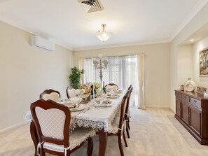Comedor con una mesa larga dispuesta para seis personas, rodeada de sillas de madera con cojines blancos.