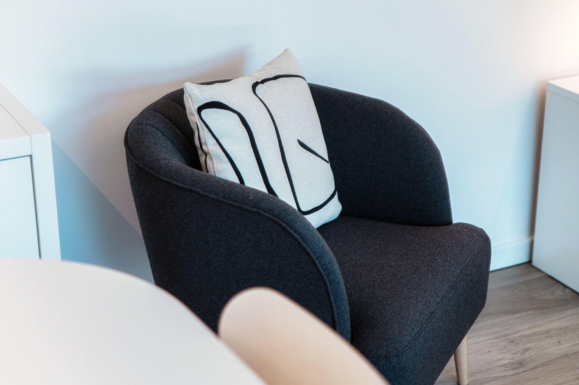 Una poltrona moderna con rivestimento scuro e un cuscino chiaro con motivo geometrico.