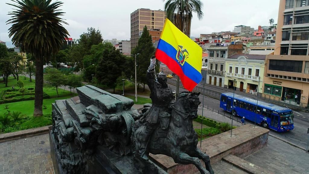 Une statue, un drapeau, un autobus et des bâtiments en arrière-plan.