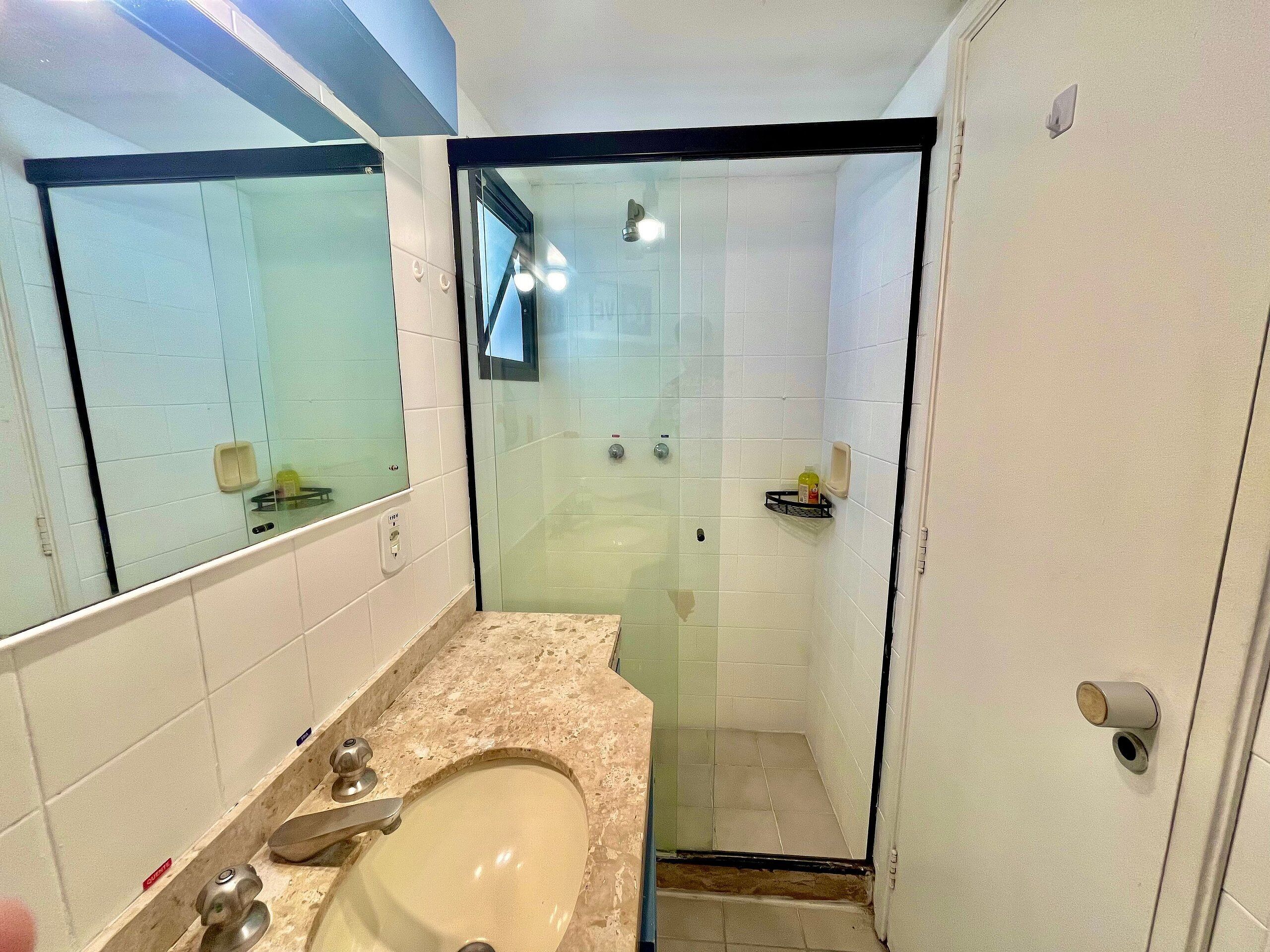 Une salle de bain dotée d’une douche à parois de verre, d’un lavabo avec un plan de travail en marbre et d’un miroir.