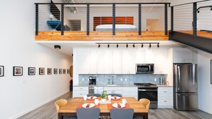 A modern kitchen with white cabinets, stainless steel appliances, and a wooden dining table with chairs. - The Lofty View:Midtown Bozeman (Bozeman)