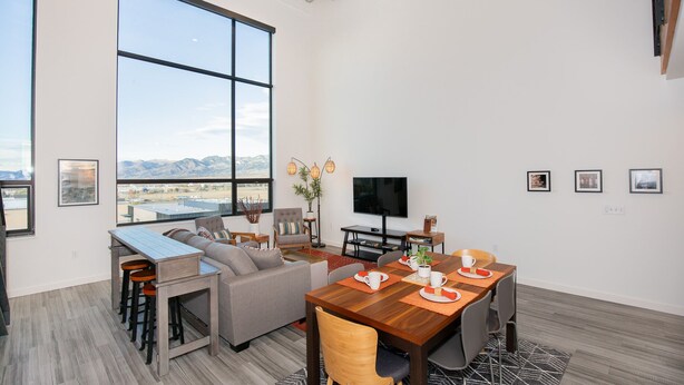 A modern living room with a large window, a dining area, and a flat-screen TV. - The Lofty View:Midtown Bozeman (Bozeman)