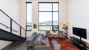A modern living room with a large window, a staircase, and a flat-screen TV. - The Lofty View:Midtown Bozeman (Bozeman)