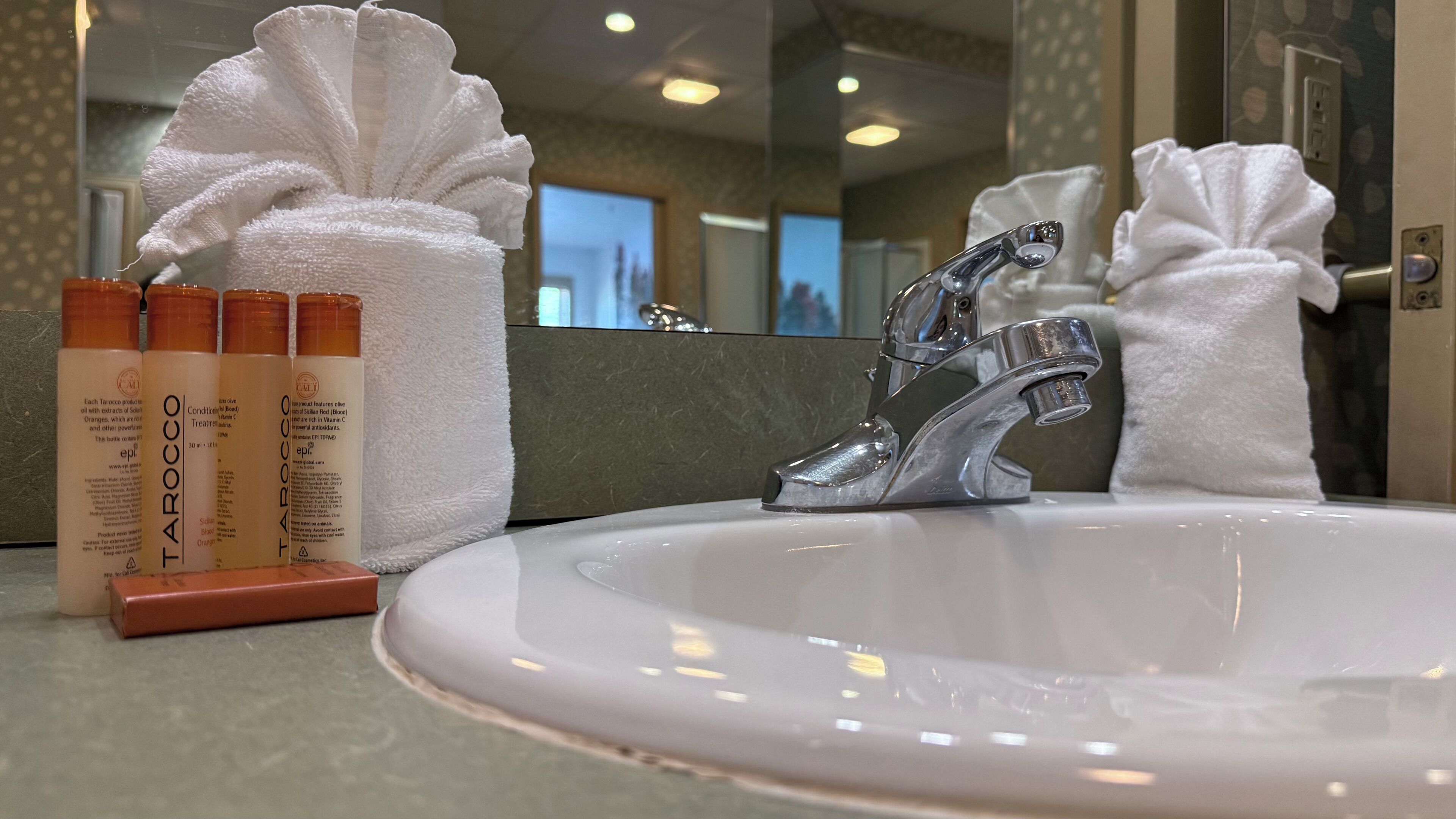 Un lavamanos de baño con un espejo, una toalla y una botella de artículos de aseo.