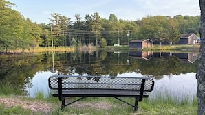 A bench by a calm lake with reflections of trees and buildings, surrounded by greenery and a clear sky. - The Willowbrook Village at Lake Harmony, a Wyndham Hotel (Lake Harmony)