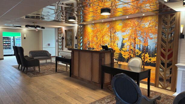 A reception area with a wooden desk, a black chair, a sofa, and a wall mural of autumn trees. - The Willowbrook Village at Lake Harmony, a Wyndham Hotel (Lake Harmony)