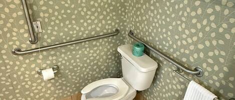 Un baño con inodoro, barras de apoyo, toallero y pared con diseño.