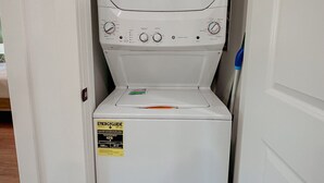 Un appareil compact, blanc, combinant lave-linge et sèche-linge, doté d’un panneau de commande, installé dans un couloir étroit.