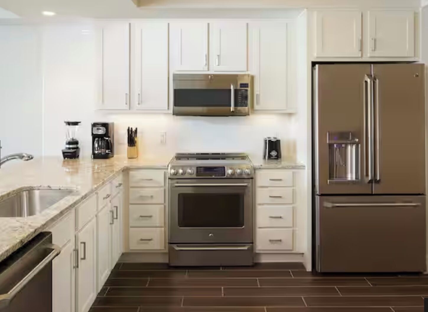 Une cuisine moderne dotée d’appareils électroménagers en acier inoxydable, de meubles blancs et d’un sol carrelé foncé.