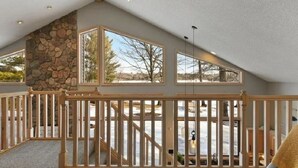A spacious room with a sloped ceiling, large windows, and a stone accent wall.