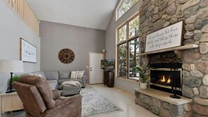 A living room with a stone fireplace, a grey sofa, a recliner, and a large window.