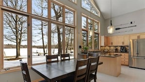 A modern kitchen with large windows, a dining area, and a view of a snowy landscape.
