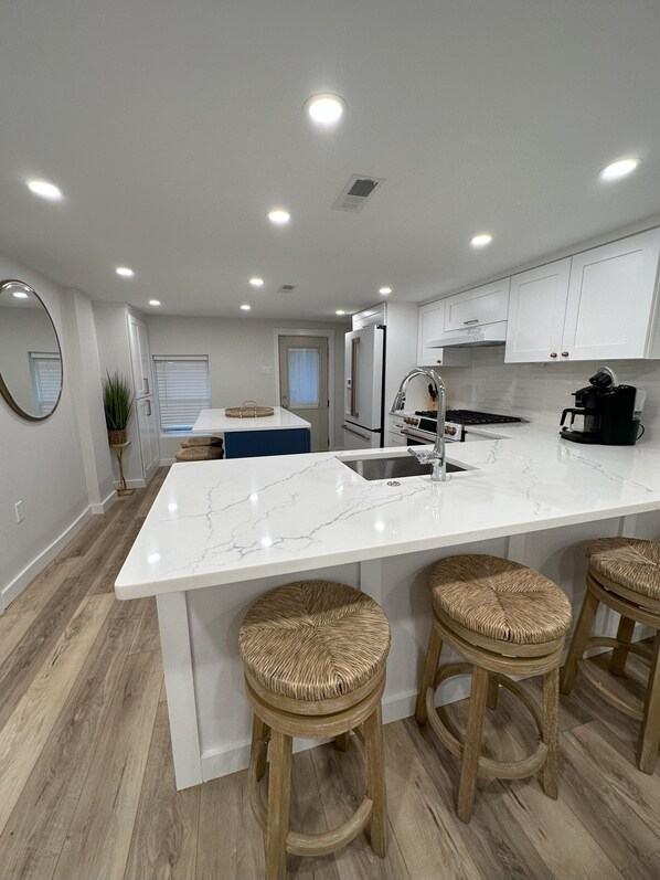 A modern kitchen with a marble island, wooden stools, and white cabinetry. - BEACH BLOCK GEM! 5BR 2 Full BA 1stFloor! Late Aug & Sept weeks still available (Ocean City)