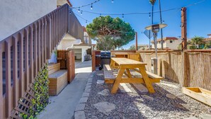 Un jardin avec une terrasse en bois, un espace barbecue et une pergola illuminée de guirlandes lumineuses.