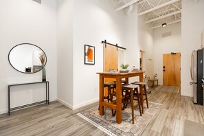 Una cocina moderna con una mesa de madera, taburetes de bar, una cafetera y un refrigerador.