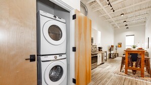 A laundry room with two stacked washing machines, a wooden door, and a kitchen area with a dining table and chairs. - Venue View: Midtown Bozeman (Bozeman)