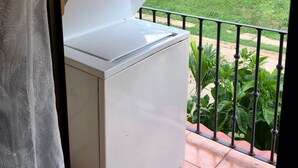 Un petit réchaud à gaz portatif, de couleur blanche, doté d’un panneau de commande, placé sur un balcon muni d’une rambarde en métal.
