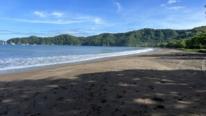 Une plage où l’on peut voir des empreintes de pas dans le sable, un ciel dégagé et des bateaux sur l’eau.