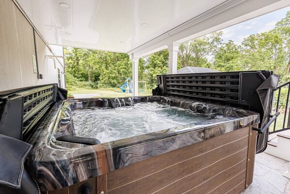 A hot tub with a wooden exterior and a metal frame, located in a covered outdoor area with a view of a playground and trees.