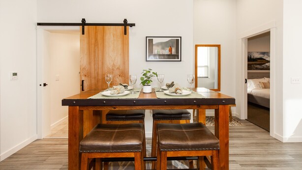 A dining area with a wooden table and four leather chairs, a sliding barn door, and a framed picture on the wall. - The Cat's Meow:Midtown Bozeman (Bozeman)