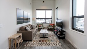 A modern living room with a sofa, coffee table, and TV, large windows, and a patterned rug. - The Cat's Meow:Midtown Bozeman (Bozeman)