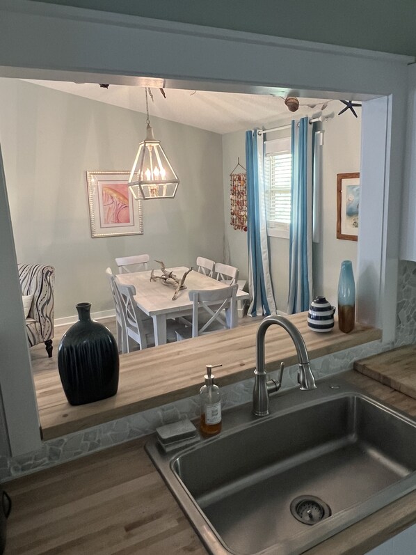 A modern kitchen with a wooden countertop, stainless steel sink, and a dining area with white chairs and a table.