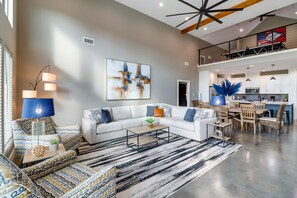 A spacious living area with a white sofa, patterned chairs, a coffee table, and a large abstract painting on the wall.
