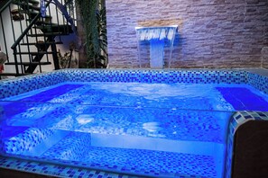 Une piscine agrémentée d’une cascade et dont le sol est recouvert de mosaïques.