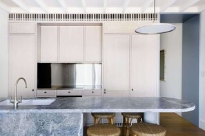 A modern kitchen with a marble countertop, stainless steel appliances, and a unique ceiling design.