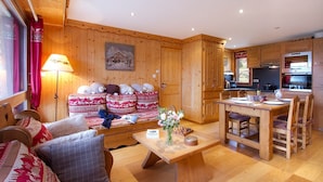 A cozy wooden interior with a sofa set, a dining table, and a kitchen area.