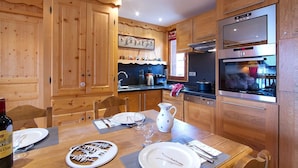 A wooden cabin-style kitchen with wooden cabinets, a Bosch oven, and a dining table set for two.