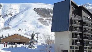 A modern building with multiple balconies and a ski resort in the background.