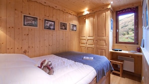 A wooden-paneled bedroom with a bed, a desk, and a window with a view of a landscape.