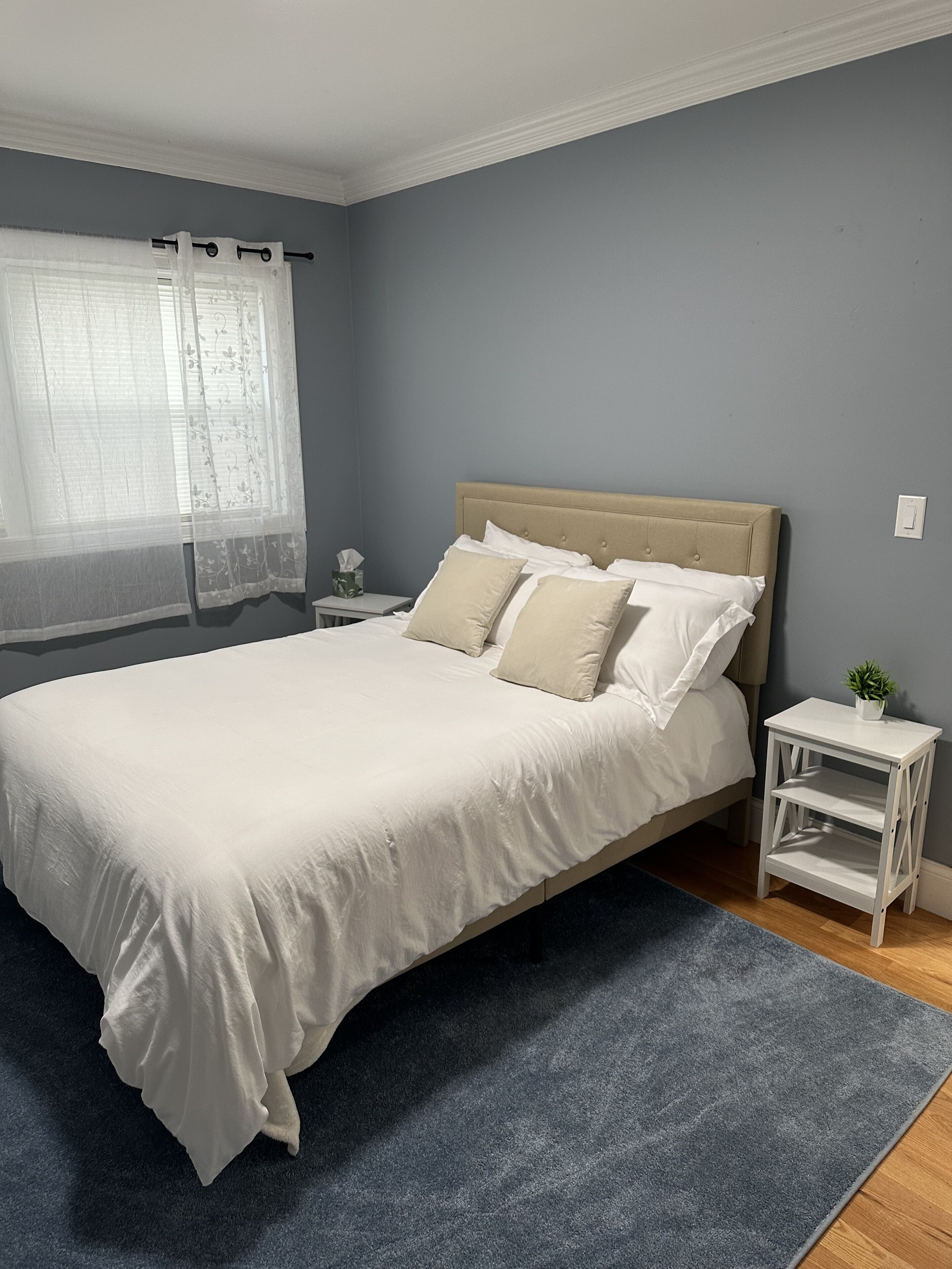 Une chambre à coucher avec un lit, une table de chevet, une petite table et une fenêtre avec des rideaux.