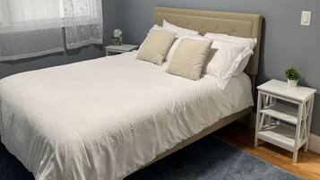 Une chambre à coucher avec un lit, une table de chevet, une petite table et une fenêtre avec des rideaux.