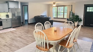 A modern kitchen with a dining area, featuring a wooden table and white chairs, a built-in oven, and a refrigerator. - Burnash Bungalow - 4 min. to Fort Drum Gate (Felts Mills)