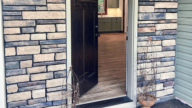 A stone facade with a dark wooden door, a doormat, and two small potted plants. - Burnash Bungalow - 4 min. to Fort Drum Gate (Felts Mills)