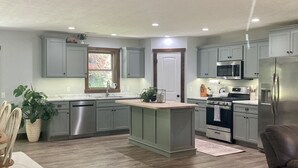 A modern kitchen with grey cabinets, stainless steel appliances, and a wooden island. - Burnash Bungalow - 4 min. to Fort Drum Gate (Felts Mills)