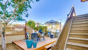 Una terraza de madera con mobiliario exterior, incluyendo una mesa y sillas, y un paraguas grande.